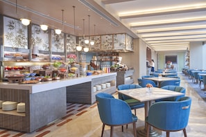 A modern restaurant with a buffet bar, blue upholstered chairs, and a long dining area.