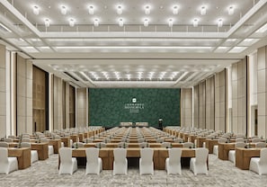 A conference room with rows of tables and chairs, a stage with a floral backdrop, and a modern ceiling design. - Shangri-La Qiantan, Shanghai (Shanghai)