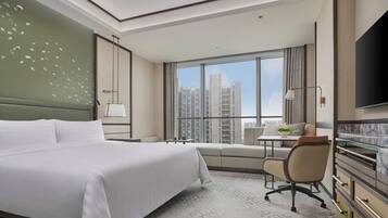 Habitación de hotel con una cama grande, un escritorio, una silla, un televisor y vistas a la ciudad.