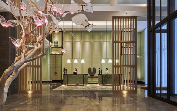 Un moderno hall de entrada con piso reflectante, una recepción y una instalación artística de árbol de vidrio.