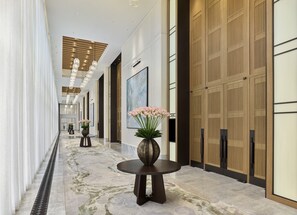 A hotel corridor with a marble floor, a round table with a vase of flowers, and wooden panel doors. - Shangri-La Qiantan, Shanghai (Shanghai)