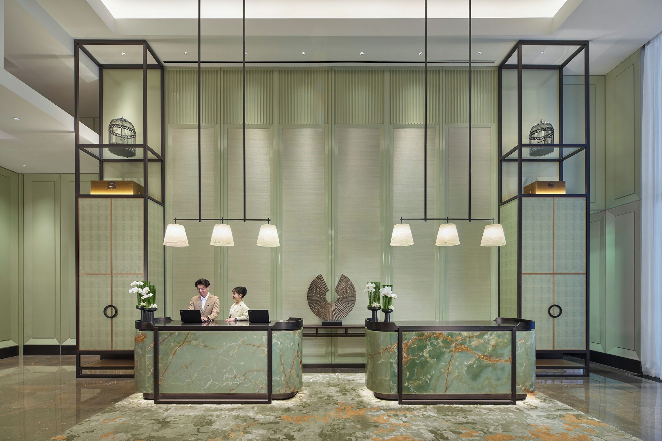 A hotel reception area with marble counters, pendant lighting, and a patterned carpet.