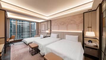 A hotel room with two beds, a desk, a chair, a small table, and a large window.