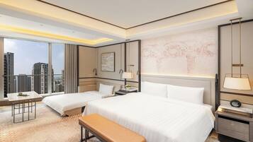A hotel room with two beds, a bench, a desk, and a large window offering a city view.