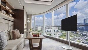 A modern hotel room with a curved view of the cityscape, a flat-screen TV, a sofa, a small table, and a lamp. - Shangri-La Qiantan, Shanghai (Shanghai)