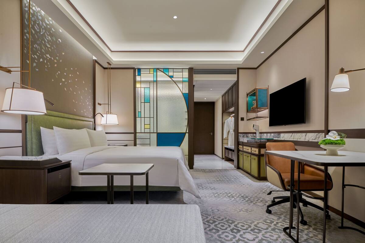 A hotel room with a bed, bedside table, lamp, desk, chair, and a TV mounted on the wall.