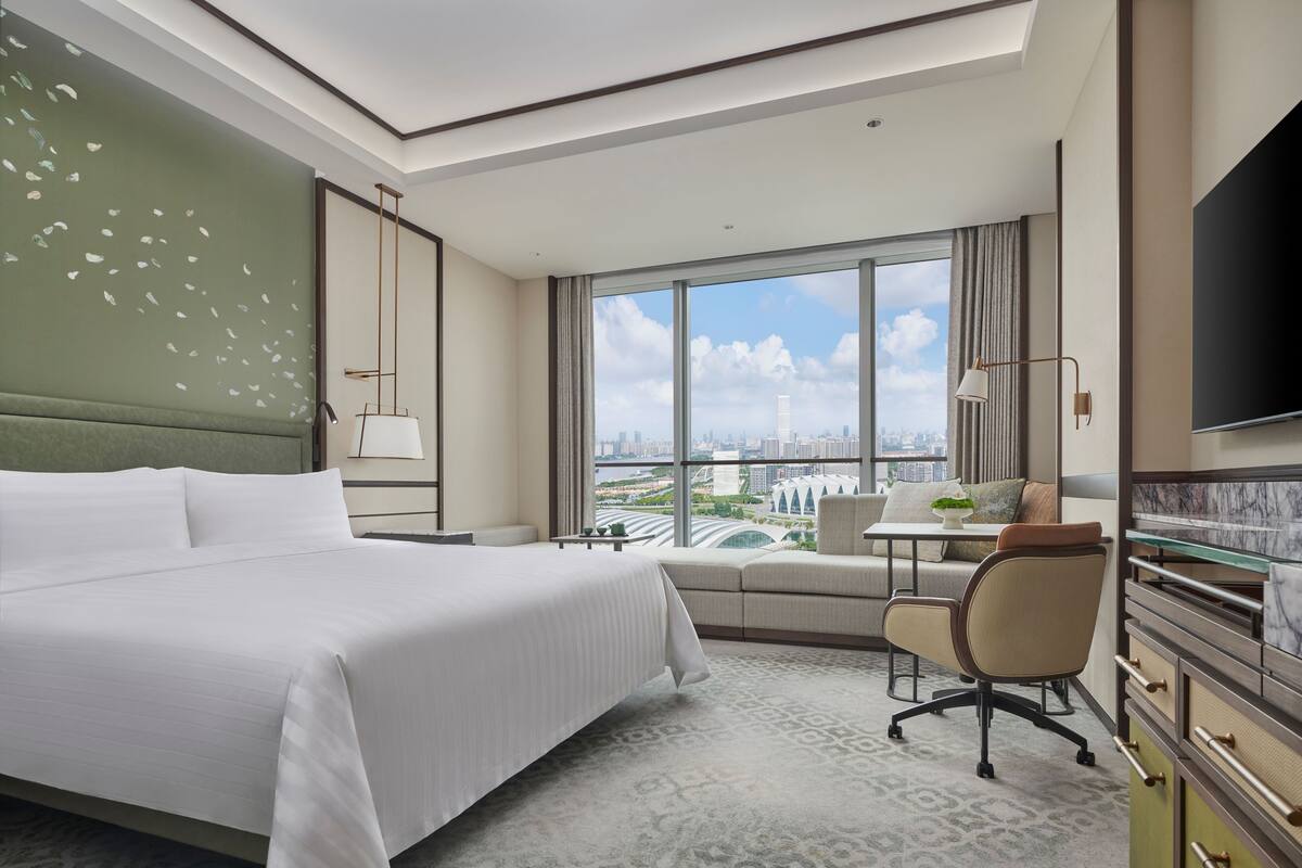 A hotel room with a large bed, a desk, a chair, and a TV.