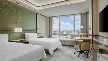 A hotel room with two beds, a seating area, a TV, and a city view.