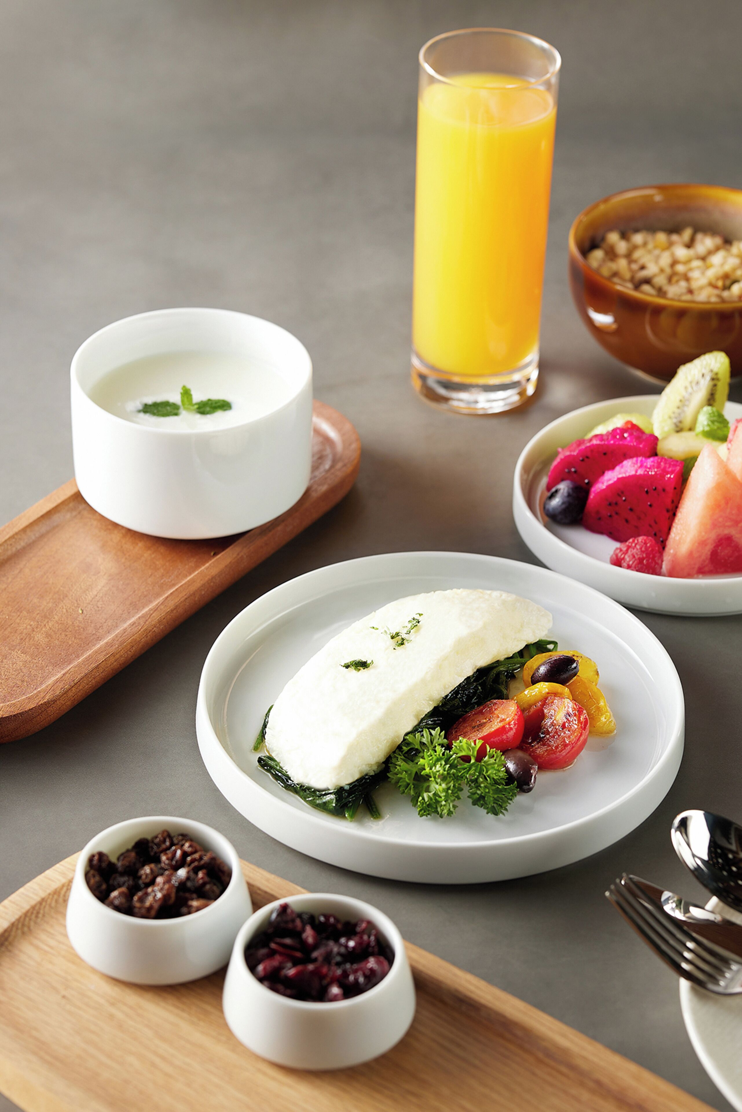 Un desayuno con un plato de comida, un vaso de zumo de naranja y recipientes pequeños con frutos rojos y nueces.