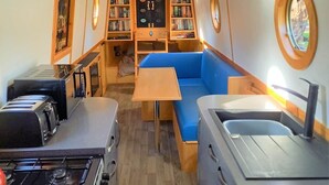 A compact kitchen with a gas stove, a toaster, and a sink. There is a blue sofa and a small table in the center.