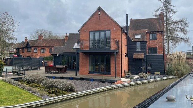 A modern house with a large balcony, a canal in front, and a garden area.