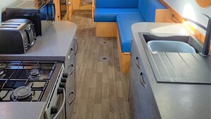A compact kitchen with a gas stove and a toaster, a blue sofa, and a wooden bookshelf filled with books.