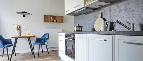A modern kitchen with white cabinets, a grey countertop, and a dining area with two blue chairs and a wooden table.
