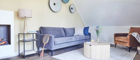 A modern living room with a grey sofa, a round coffee table, a fireplace, and a wall-mounted clock.