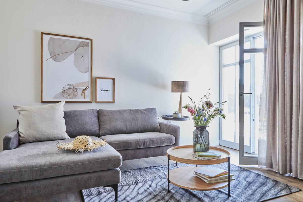 A modern living room with a grey sofa, a round coffee table, and a large window with curtains.