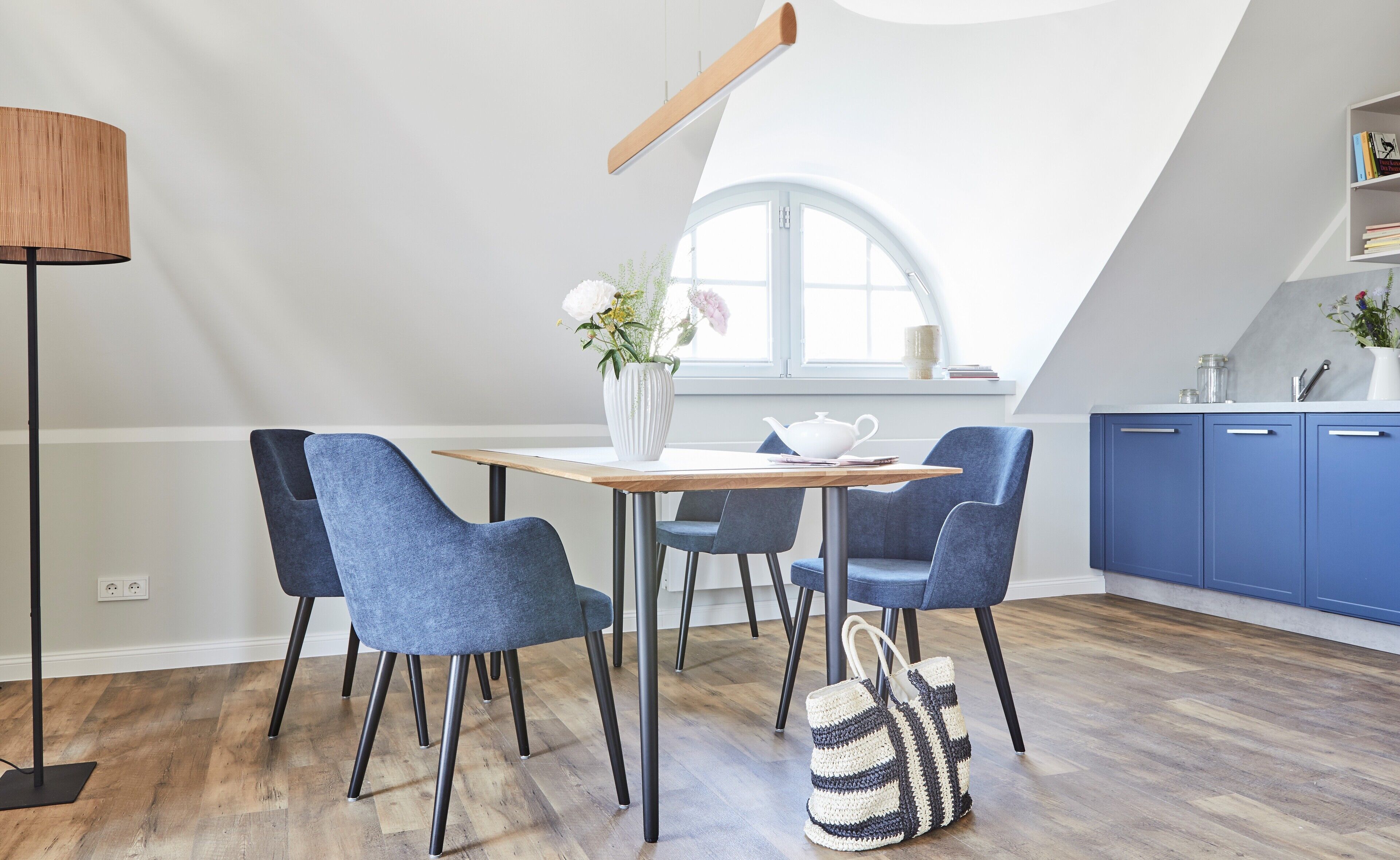 A modern kitchen with a dining table, chairs, a hanging light fixture, and a window with a view.