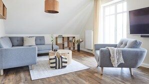 Una sala de estar moderna con un sofá y un sillón grises, una mesa de centro de madera y una lámpara colgante.