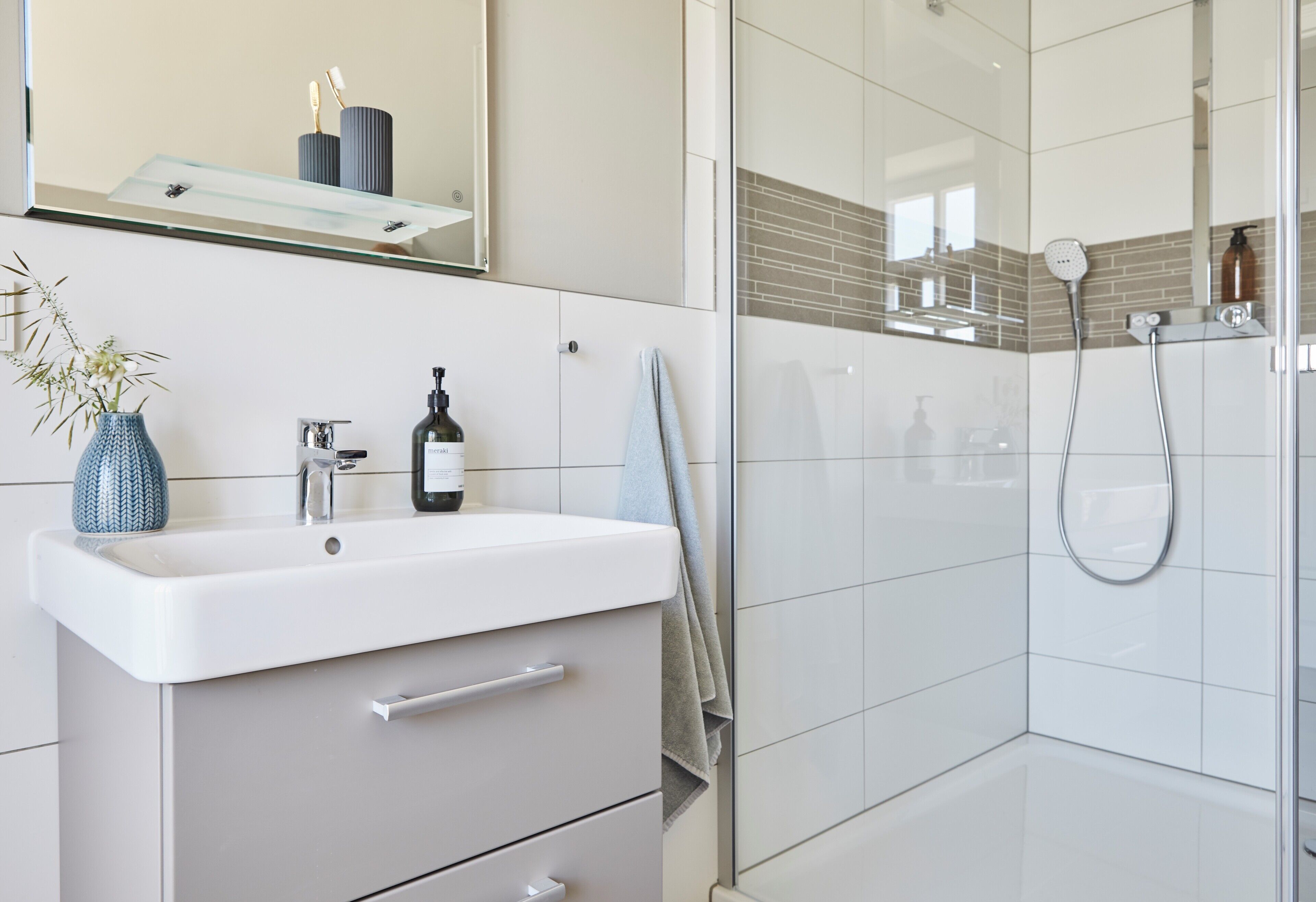 A modern bathroom with a white sink, a mirror, and a shower area.