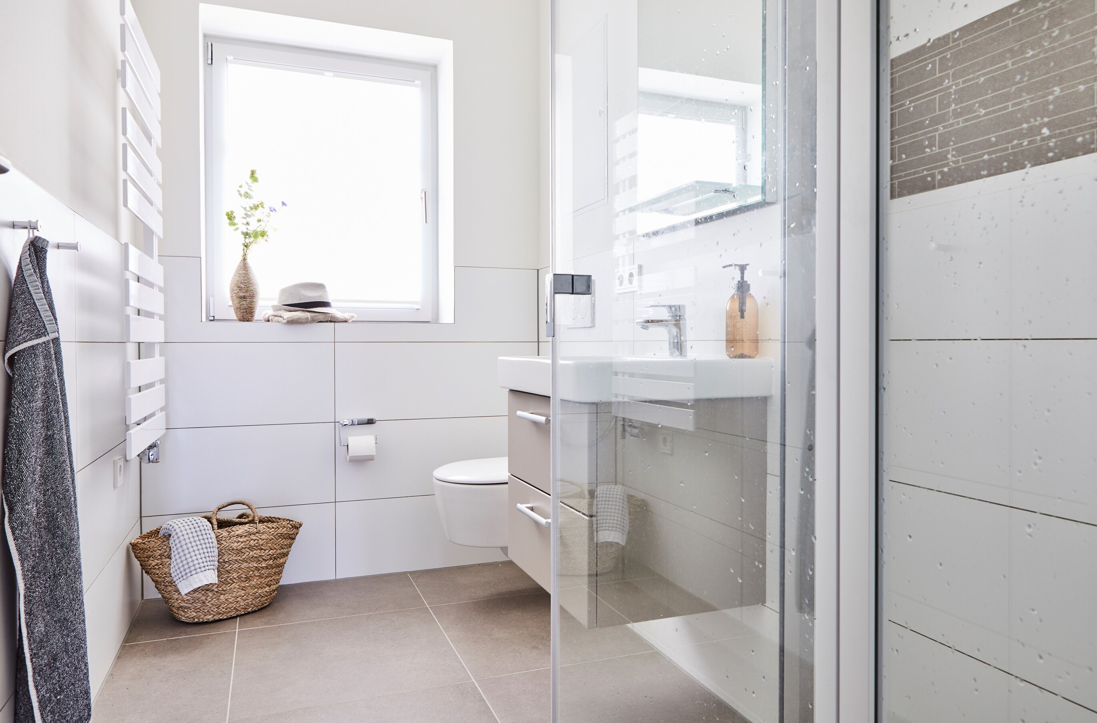 A modern bathroom with a toilet, a glass shower enclosure, a sink with a mirror, and a window providing natural light.