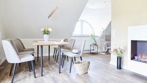 Un comedor moderno con una mesa de madera, sillas grises tapizadas, un jarrón blanco con flores y una chimenea encendida.