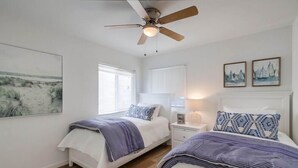 A bedroom with two beds, a ceiling fan, a nightstand with a lamp, and artwork on the walls. - Convenient Ground Level * Steps to Ocean * Outdoor Patio (San Diego)