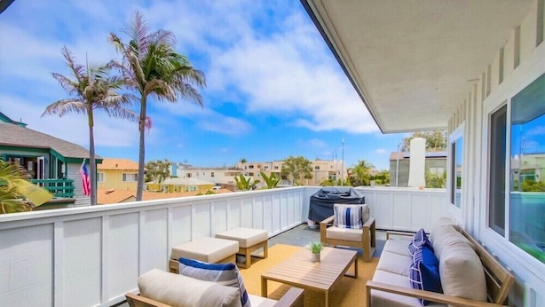 A balcony with wooden furniture, a grill, and a view of palm trees and buildings. - Steps to Ocean + Bright Top Level Unit + Sun Deck (San Diego)