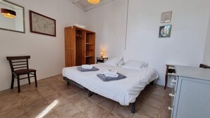 Quarto com cama, guarda-roupa de madeira, cadeira, escrivaninha e mesa de cabeceira com abajur.
