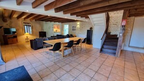 A spacious living area with a wooden dining table, black chairs, a sofa, and a TV. There is a staircase leading to an upper level. - The Plough House with 4 bedrooms (Saint-Just-Luzac)