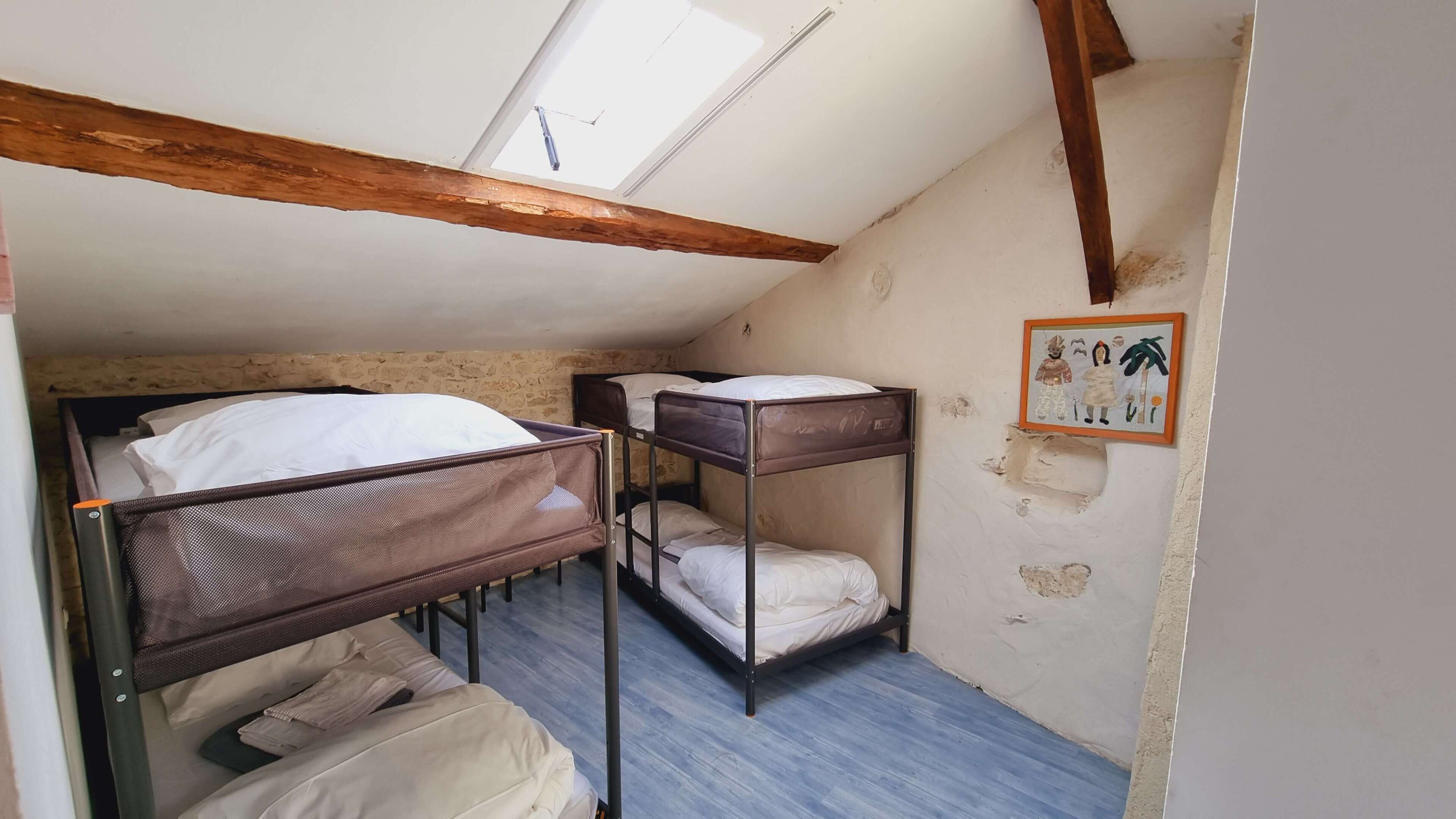 Une chambre de dortoir avec des lits superposés, une poutre en bois au plafond et un petit tableau accroché au mur.