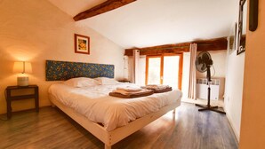 A bedroom with a wooden bed, a nightstand with a lamp, a fan, and a window with curtains. - The Plough House with 4 bedrooms (Saint-Just-Luzac)