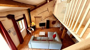 Ein rustikaler Raum mit einer Couch, einem Fernseher, einer Lampe und einem mit Vorhängen drapierten Fenster.