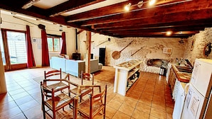 Eine rustikale Küche mit Steinwand, Holzbalken, Kamin und Essbereich mit Stühlen und Tisch.