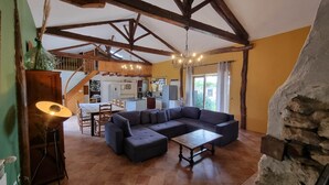 A cozy living room with a large sectional sofa, a dining table, and a kitchen in the background.