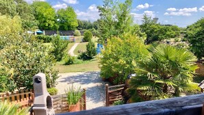 A view from a balcony overlooking a garden with a pathway, a wooden fence, and a stone structure.