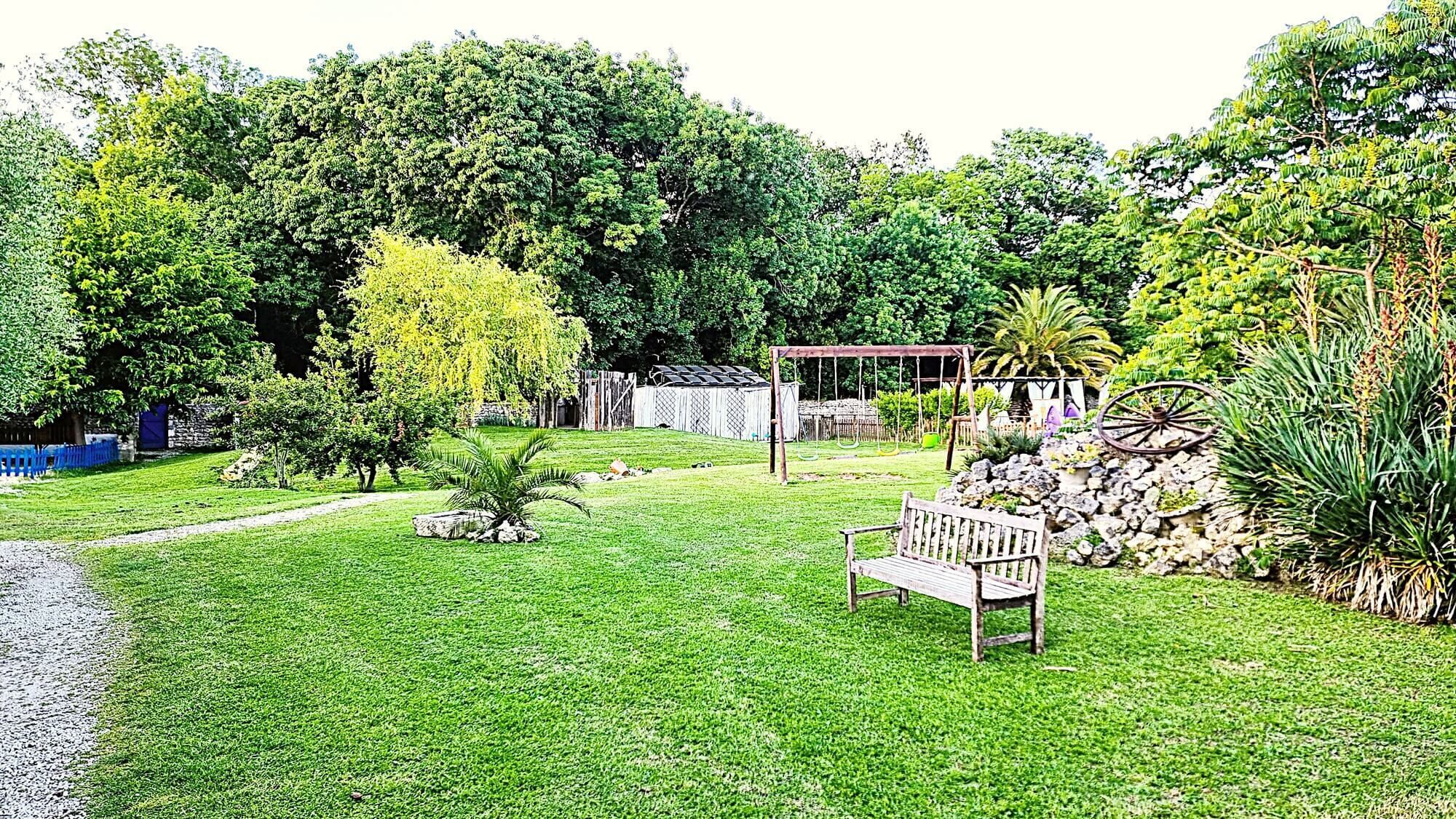 A well-maintained garden with a wooden bench, a gazebo, and various plants.
