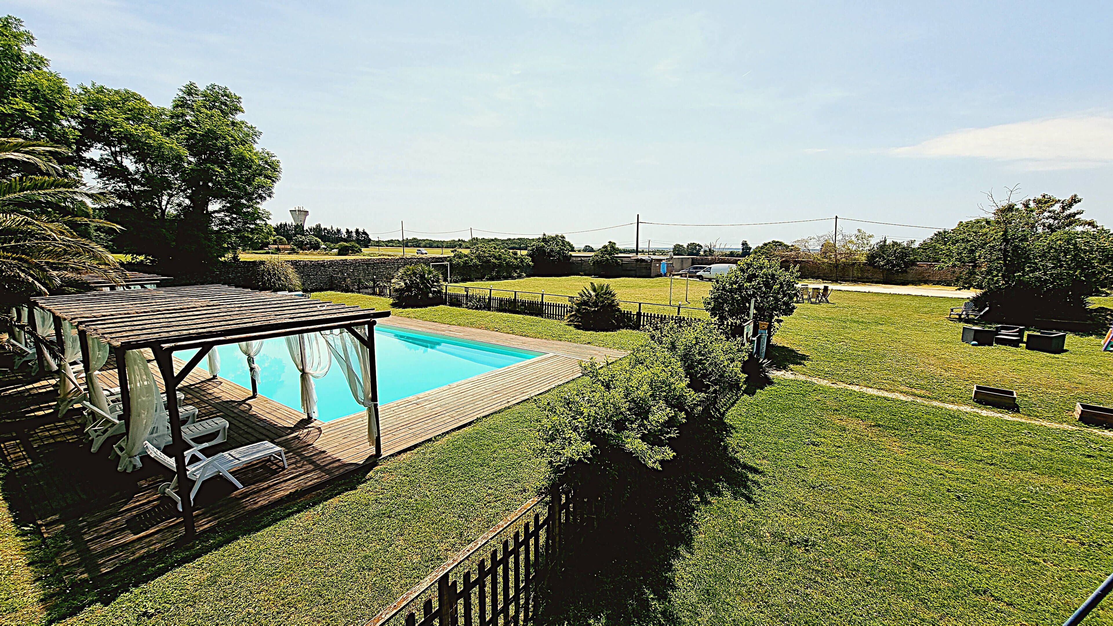 En have med swimmingpool, træterrasse og overdækket siddeområde.