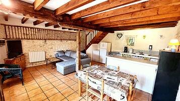 A rustic kitchen with a dining table, a sofa, and a television in a cozy living area with exposed wooden beams.