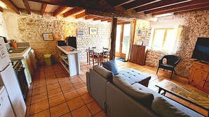 A rustic kitchen with a dining area, stone walls, and a sofa. - La Mangeoire 2 bedroom gîte (Saint-Just-Luzac)