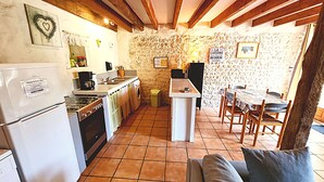 A kitchen with a stove, sink, and a dining area with a table and chairs. - La Mangeoire 2 bedroom gîte (Saint-Just-Luzac)