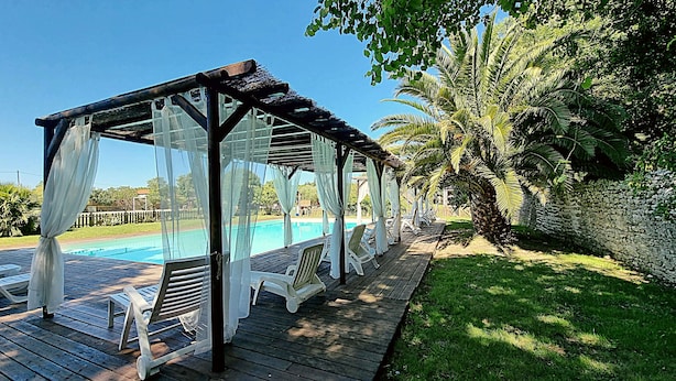 Eine Holzterrasse mit Pool, weißen Stühlen und einer Pergola mit durchsichtigen Vorhängen.