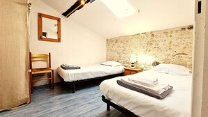 Ein Zimmer mit zwei Betten, einem Holzstuhl, einem Nachttisch mit Lampe und einem Spiegel an der Wand.