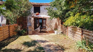 Ein Haus aus Stein mit einem Ziegeldach, einem Holzzaun und einer gepflasterten Terrasse mit Tisch und Stühlen.
