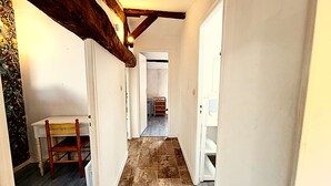 Un couloir étroit avec une chaise en bois, une petite table et un escalier menant à une autre pièce.