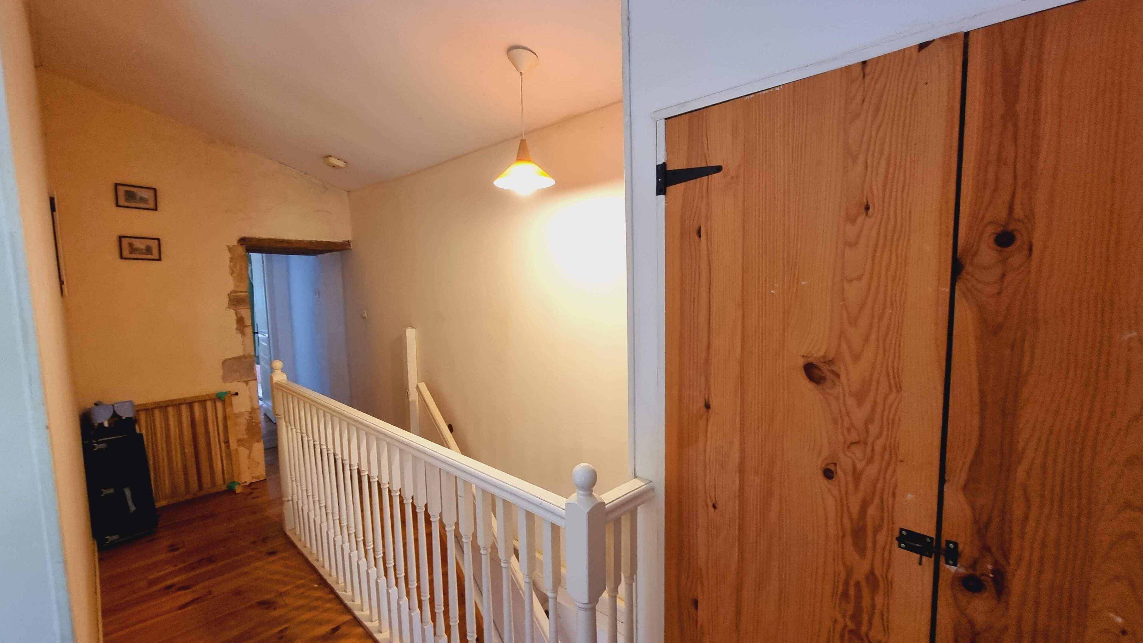 Un couloir doté d’un plancher en bois, d’une rambarde blanche et d’une porte en bois.