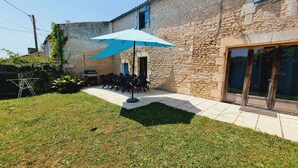Ein Steinhaus mit einer Terrasse, auf der ein Grill und Sitzgelegenheiten für draußen stehen.
