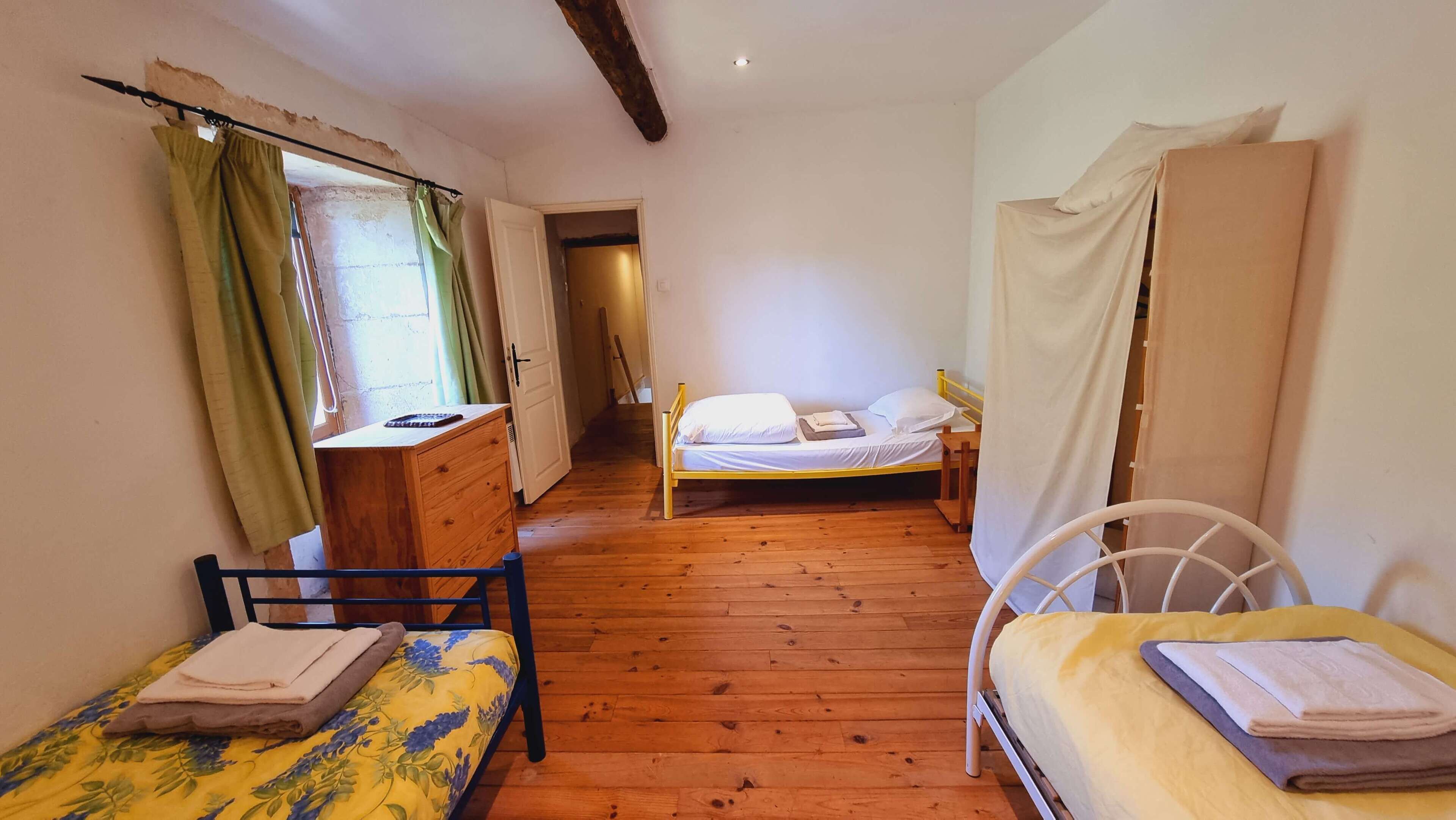 Una habitación con suelo de madera, dos camas, un escritorio y una silla.