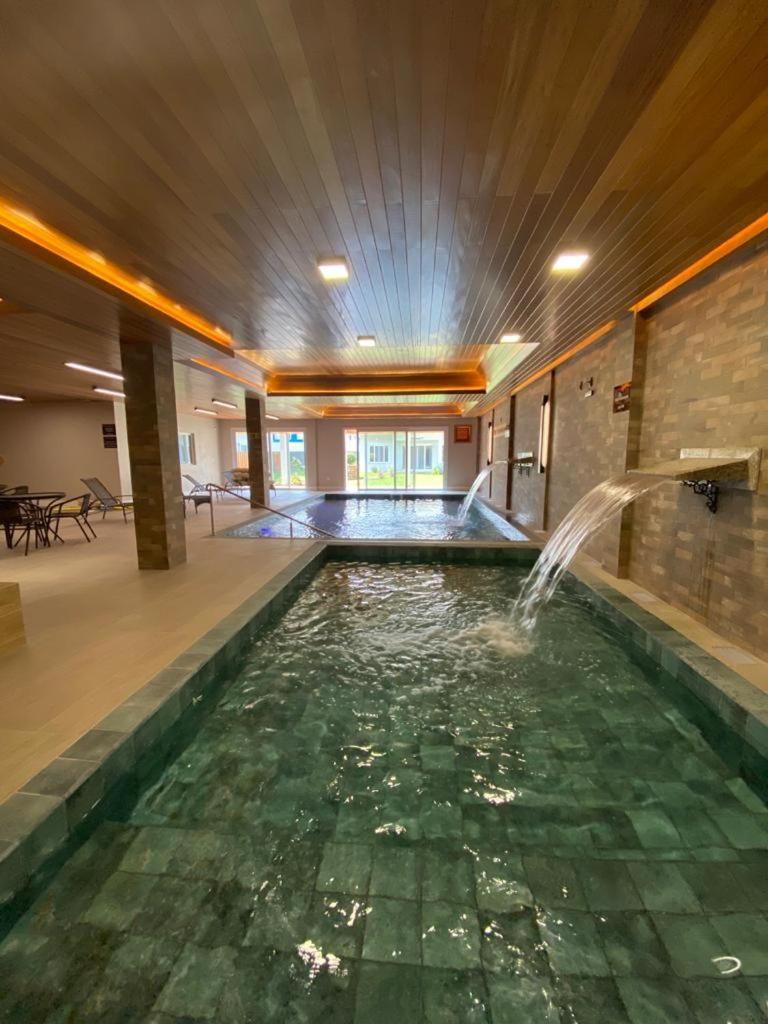 A swimming pool with a waterfall feature, surrounded by a tiled floor and wooden ceiling.