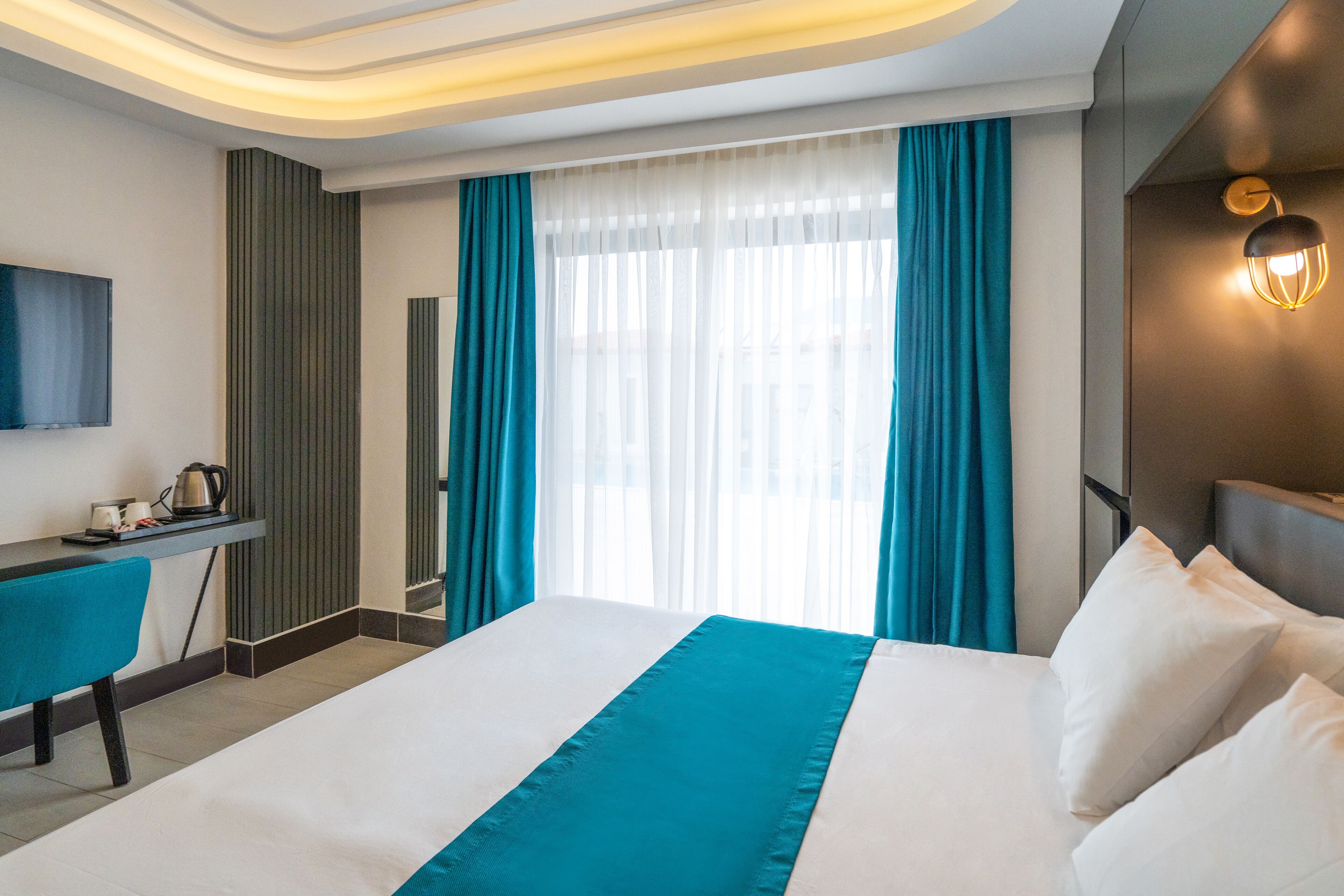 A hotel room with a bed, a desk, a chair, a television, and a window with curtains.