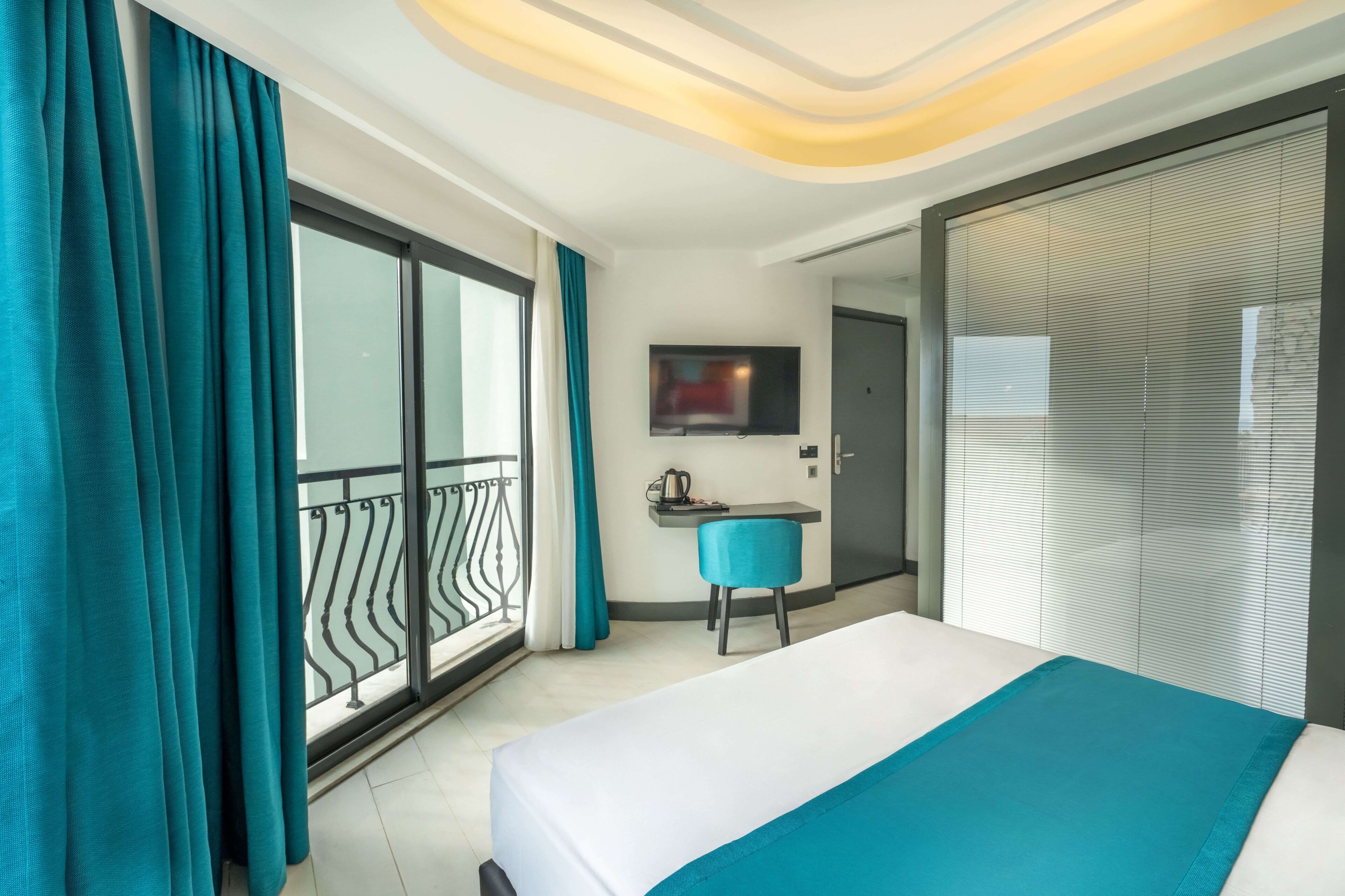 Una habitación de hotel con cama, escritorio, silla, televisor y puerta corrediza.