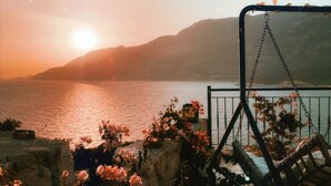 A patio with a swing chair overlooking a body of water and mountains during sunset. - GÜMÜŞ YAZAR  HOTEL (Kas)